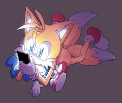 Size: 908x769 | Tagged: safe, artist:41waysu, miles "tails" prower, sonic the hedgehog, 2025, grey background, holding something, looking at something, lying on front, phone, simple background, smile, solo, stuffed animal